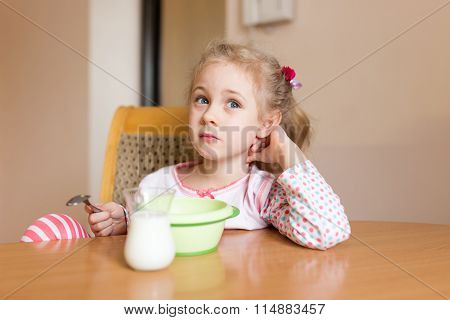 Little girl having breakfast at home. Milk mustache