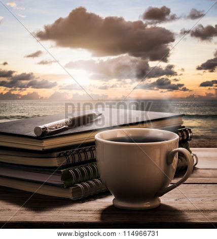 Hot Coffee With Notebooks And Pen On Wooden Table With View Of The Sea
