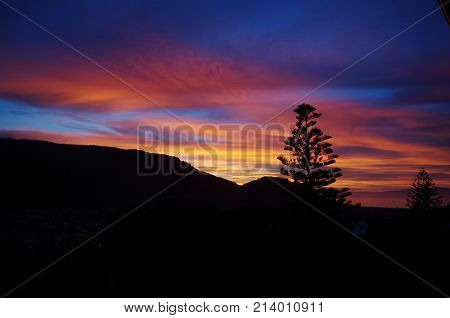 Fire in the Sky at Sunrise with lonely tree silhouette on black mountain