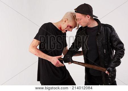 Two young guys in black are fighting. The guy in the cap beats a wooden bat in the stomach to another guy. Isolation.