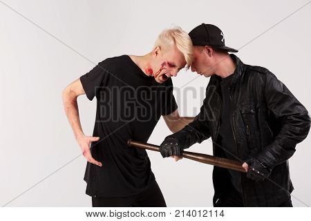 A dangerous guy in a black cap beats a defenseless guy with a battered face and bruises with a wooden bat. Isolation.