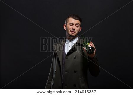 A man on a black background, retro style, holds a bottle of alcohol in his hand, screwing up his eyes, looks into the bottle, a cigarette sticks out behind his ear.