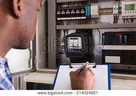 Close-up Of Male Technician Writing On Clipboard In Front Of Fuse Box