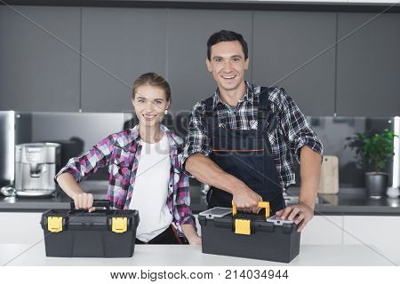 A man and a woman plumber will be cheated in the kitchen. They have just successfully repaired the sink for the customer. Next to them is a black box with a tool.