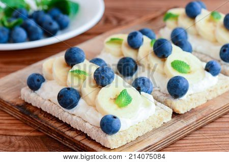 Cottage cheese, bananas and berries sandwiches. Diet sandwiches with crispbread on wooden board. Closeup