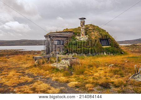 Cabin with turf roof near Hardangervidda National Park with a lake in the background, Hordaland county, Norway.