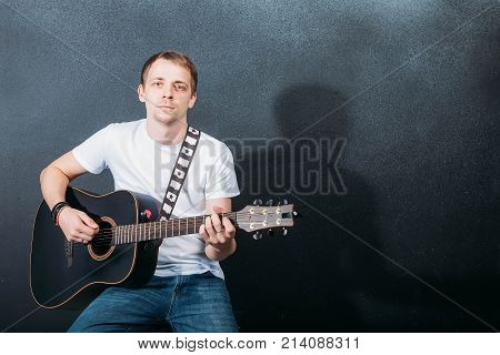 Cheerful young guitarist. Cheerful handsome young man playing guitar and smiling while sitting at chair