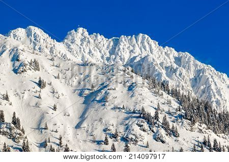 High mountain with summit cross under deep snow on sunny winter day. Rauhhorn, Allgau, Bavaria in Germany.