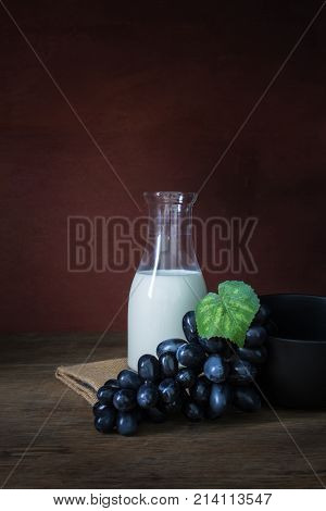 Bottle of milk with grapes and black wowl on wooden floor in still life shot