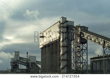 a fragment of a modern industrial enterprise with several silos for storage of loose materials and an inclined covered belt conveyors