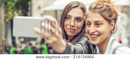 Happy girl friends taking selfie photos in the street. Internet and social media