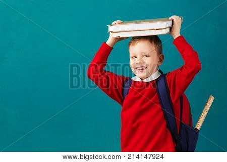 Cheerful Thoughtful Little School Boy In School Uniform With Backpack And Big Pile Of Books Standing