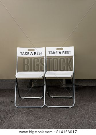 Pair of folding plastic chairs with the message Take a Rest engraved on the backrest