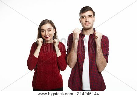 Happy ecstatic young European man and woman in love keeping clenched fists at their faces cheering being excited with success victory or good luck. Overjoyed couple celebrating good positive news
