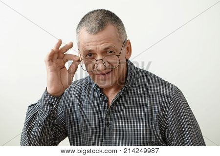 Headshot of attractive smoothly shaven 60 year old retired man with grey hair adjusting his stylish eyeglasses going to watch series on TV or read newspaper. People age optics and eyewear concept
