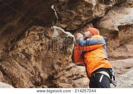 Hipster is an alpinist in the era of climbing a beautiful rock without insurance and helmet. A mountaineer in a knitted cap and down jacket with a bag for magnesia and chalk on a belt and carabiners warms his hands before another approach to the rock. The