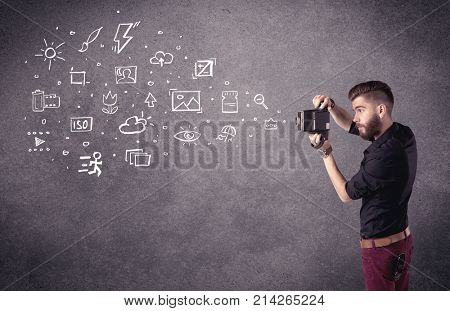 An elegant hipster guy trying to use a vintage camera with camera settings icons drawn on wall, like flash, white balace or ISO value concept