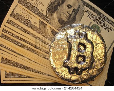 Bitcoin real metal coin is on one hundred dollars bills or banknotes. It means hot price or value and high exchange rate of crypto currency on market. It also means investments with financial risk