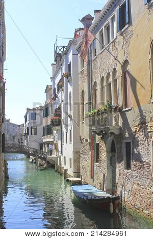 VENICE - JUNE 19 2011: One of the many channels of the ancient city. Sleeping gondolas are shaking sleepily. Deteriorated buildings are reflected in the water. In the city noon.