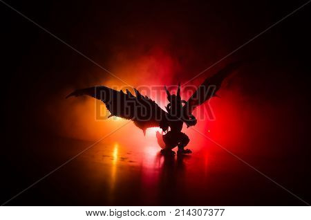 Silhouette Of Fire Breathing Dragon With Big Wings On A Dark Orange Background. Empty Space