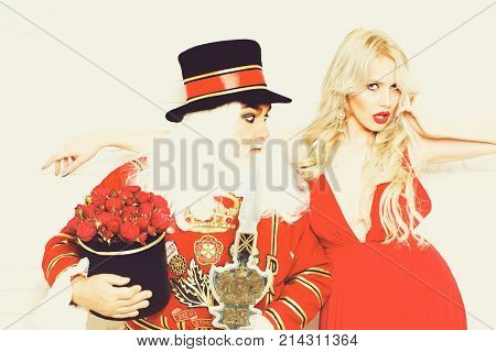 Curious senior man beefeater yeomen warder in uniform and pretty girl young sexy blond woman on white brick wall