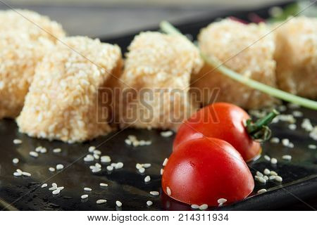 Cropped close up of delicious cheese rolls with sezam served on a black plate with cherry tomatoes and greens copyspace menu food eating gourmet tasty menu delicacy concept.