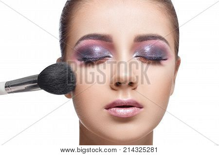 Closeup portrait of beautiful young woman with perfect skin and pink makeup. Girl applying cosmetic using makeup brush. Isolated on white. Perfect make up. Concept of beauty and fashion
