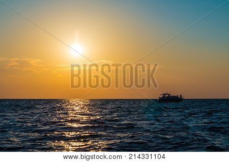 The setting sun over the sea and the motorboat sailing in the distance