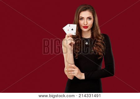 Beautiful caucasian woman in black dress with poker cards gambling in casino. Studio shot on red background. Poker. Two Aces in Hand