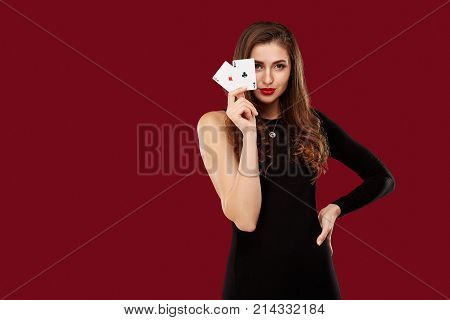 Beautiful caucasian woman in black dress with poker cards gambling in casino. Studio shot on red background. Poker. Two Aces in Hand