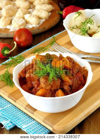 Meat stewed in tomato sauce. Porkolt, Hungarian cuisine meal. Gnocchi, a type of dumplings in the background