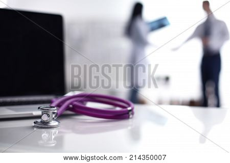 Laptop and medical stethoscope on the desk , doctors standing in the background.