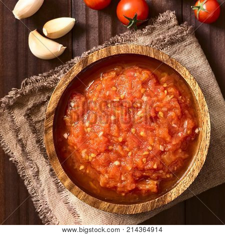 Homemade traditional Italian marinara or pomodoro tomato sauce made of fresh tomato garlic dried oregano and salt served in wooden bowl with ingredients on the side photographed overhead on dark wood with natural light (Selective Focus Focus on the top of