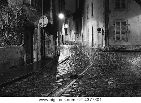 A night scene captures an empty street in the city of Beaune in France where the wet cobblestones are bright with reflected light from the street lights. (Scanned from black and white film.)