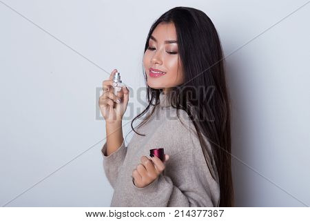 Beautiful young girl use perfume and smiling while standing in front of white background. Asian sexy girl perfume oneself, close her eyes and exited of new smell