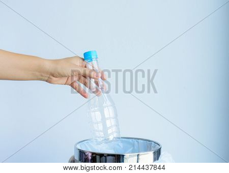 Women hand throwing empty plastic bottle into a trashbin.