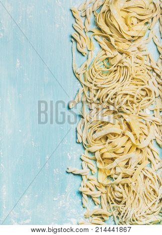 Various homemade fresh uncooked Italian pasta with flour on blue wooden background, top view, copy space,