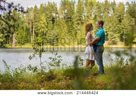 Hot couple in the summer forest enjoying nature. Beautiful girl in a white dress. Outdoors. Wedding love story. Having fun. Boyfriend gives his girl a kiss.