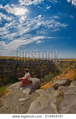 Young woman sitting on the edge of Kasagh river gorge near Saghmosavank monastery
