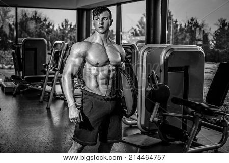 Handsome man with big muscles, posing at the camera in the gym. Muscular man in blue shorts and with bare chest. Black and white