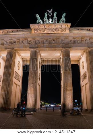 Historic Brandenburg Gate long exposure blurred unrecognizable people and and four horses bronze statue illuminated at night against dark black sky