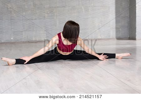 Female gymnast work out in studio. Young slim girl doing splits on studio background. Young dancer stretching in studio.