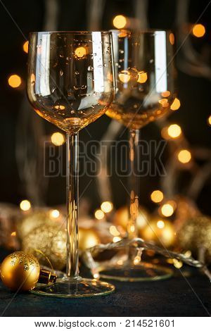 Two glasses for wine and golden Christmas balls against a background of blurred golden lights. Shallow depth of field.