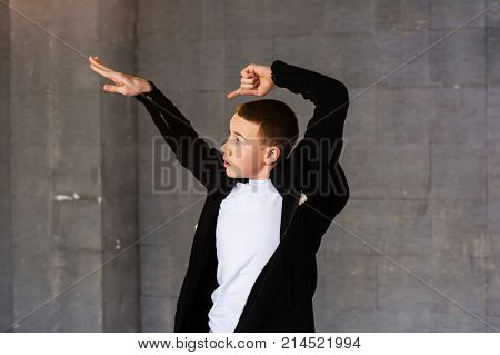 Young dancer posing on grey background. Young handsome dancer boy performing dance element in studio. Guy dancing modrern dance.