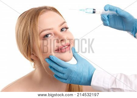 The doctor's hands in a white coat and medical gloves hold a syringe near the face of a young and attractive woman. Isolated on white background.