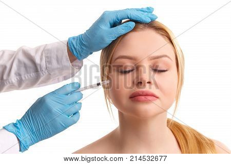 The doctor in medical gloves injects on the cheek of a beautiful young woman. Isolated on white background.