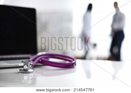 Laptop and medical stethoscope on the desk , doctors standing in the background.