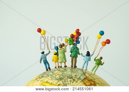 miniature people figure back view of happy family holding balloons standing on globe as looking into the universe or happy american family concept.