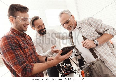 Three men set up a self-made 3d printer to print the form. They are checking the 3d model of the tablet. Men discuss the nuances and difficulties of printing the chosen model.