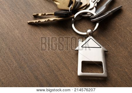 Bunch of keys on a house shaped keychain at wooden table background. Concept for real estate or renting home with copy space